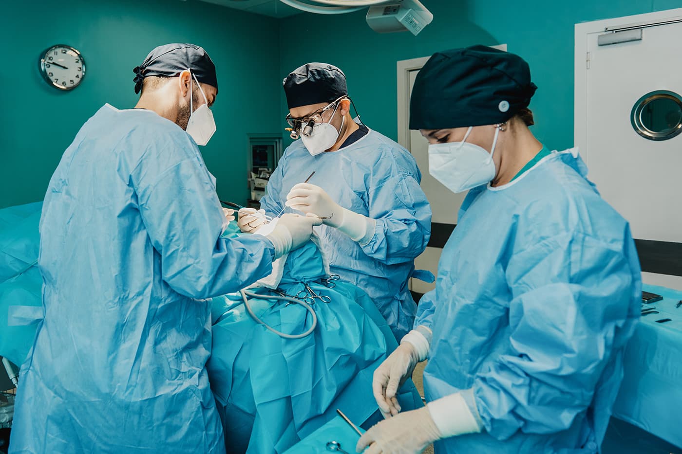 Three surgeons in masks and gowns performing a procedure in an operating room.